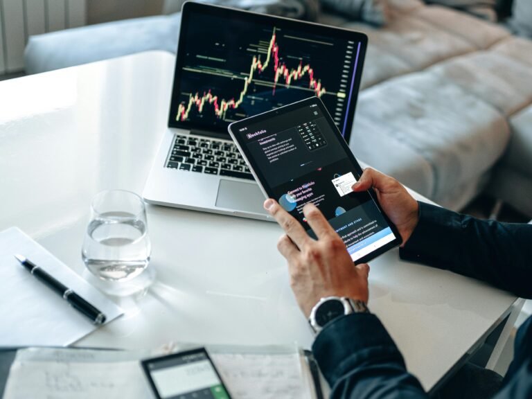 Person analyzing digital market trends on tablet with laptop showing financial charts.